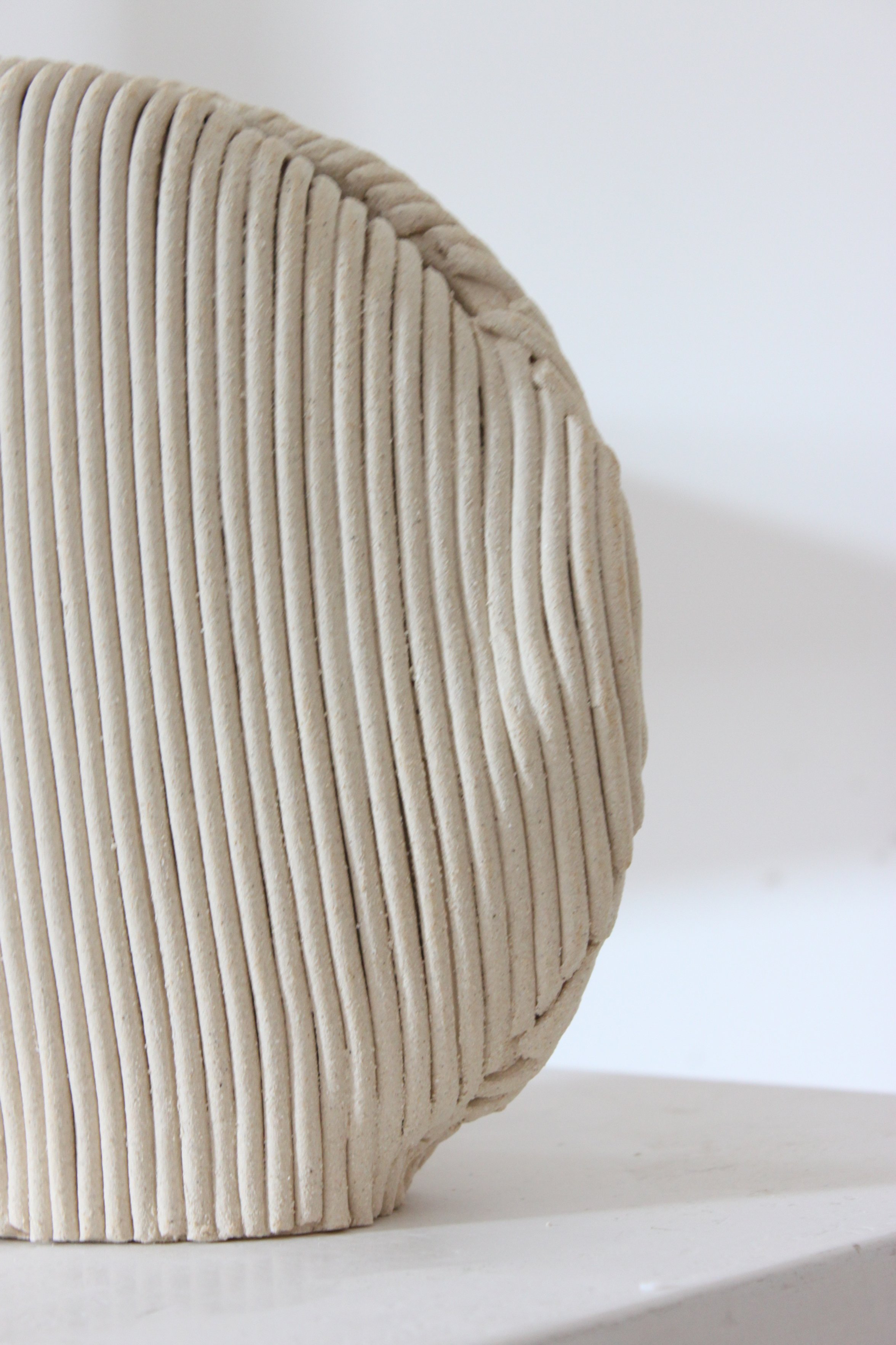 Une image d'un objet rond en bois avec des rainures verticales, placé sur une surface blanche.