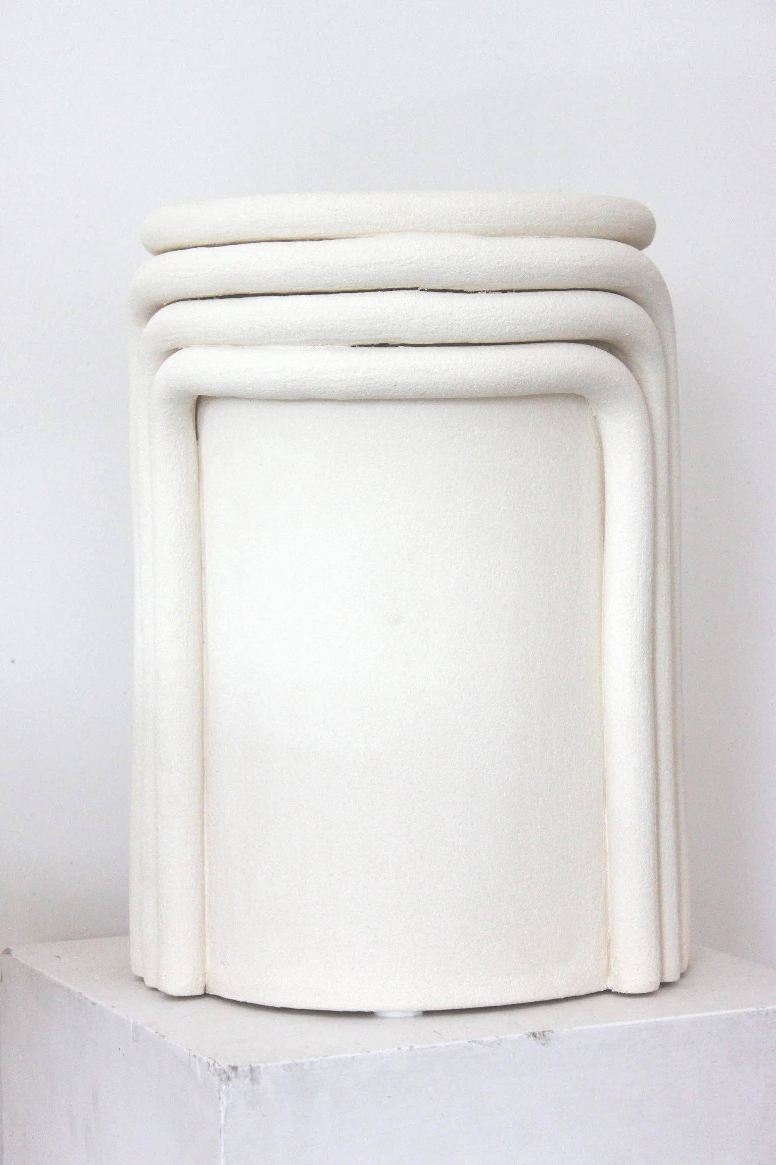 Pyramide de quatre plaques blanches arrondies empilées, posée sur une surface blanche, photographiée en gros plan contre un fond blanc.