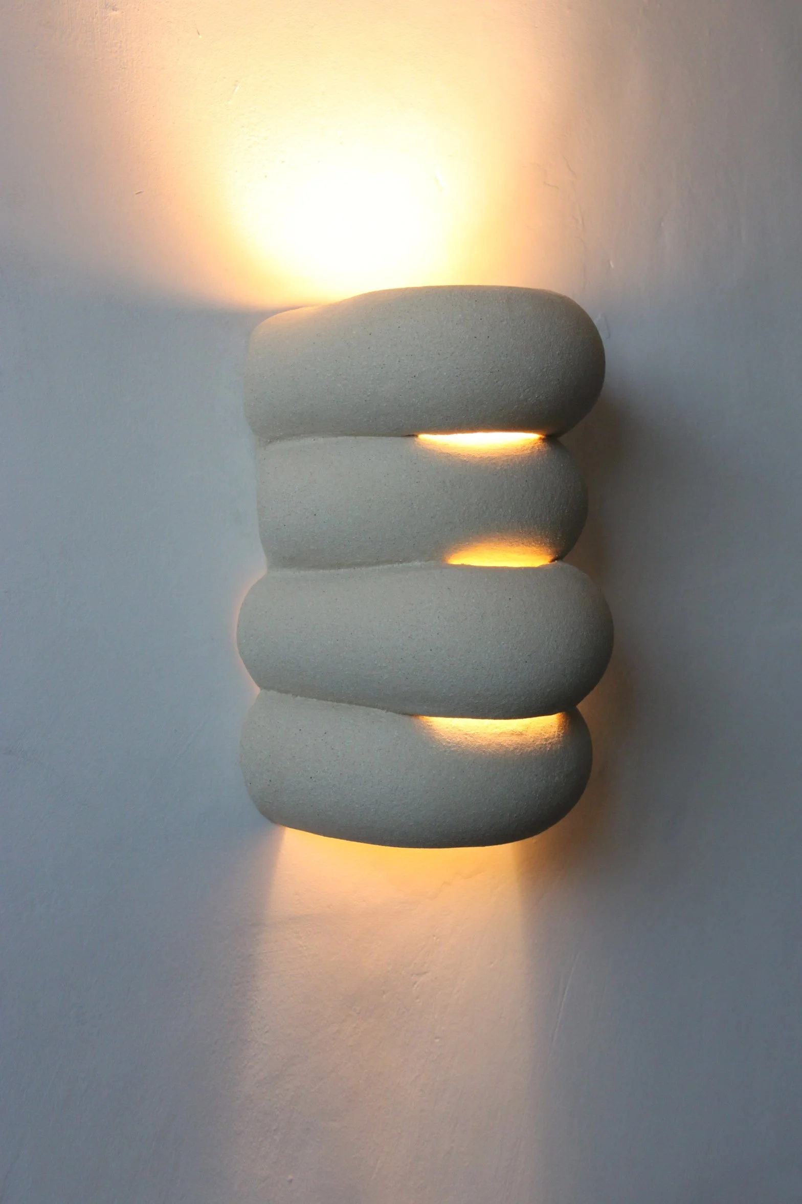 Applique murale en pierre beige avec lumières intégrées émettant une lumière douce.