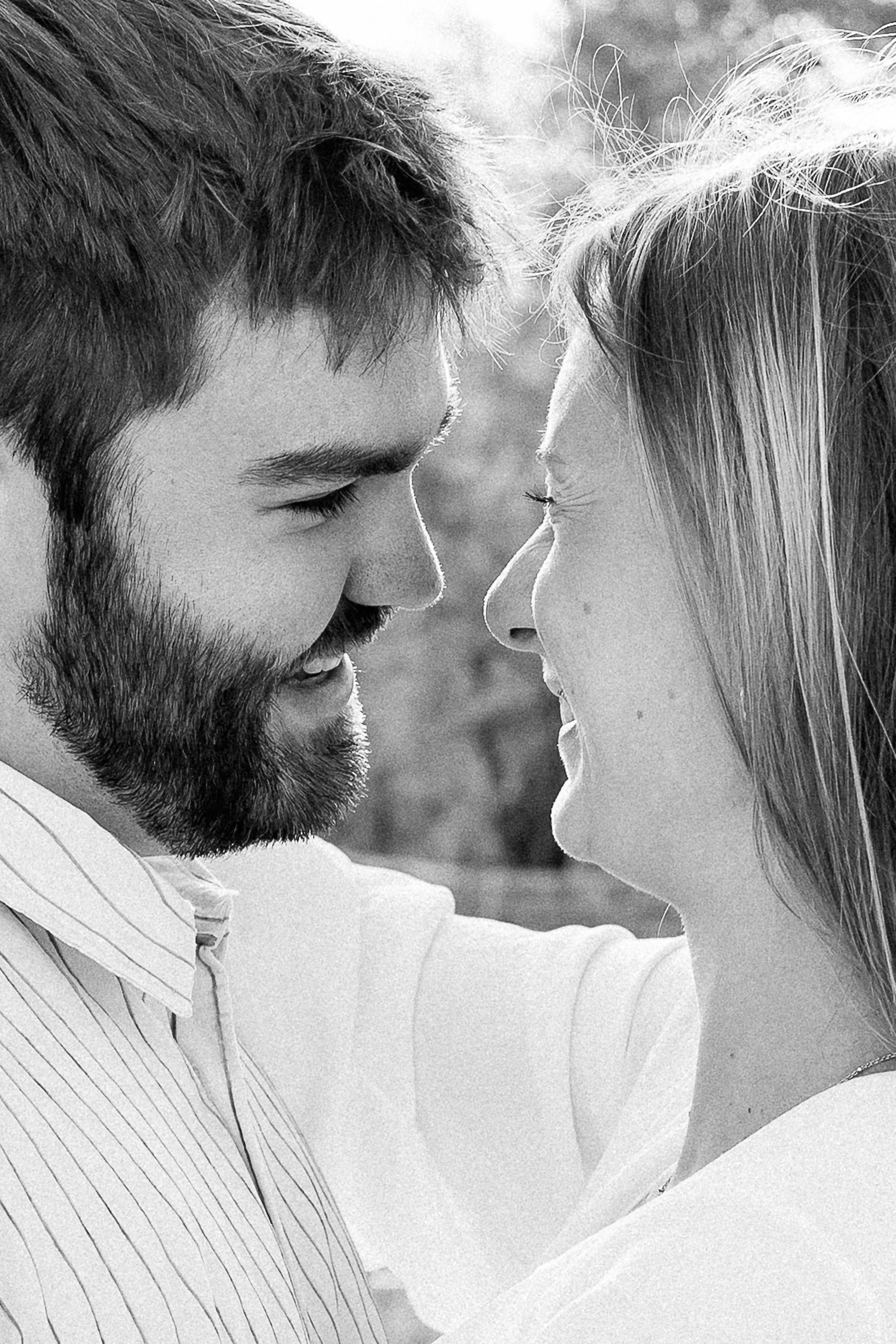 A black-and-white close-up portrait of a couple smiling with their foreheads nearly touching. Both are laughing softly while looking into each other’s eyes, creating an intimate and joyful moment with a softly blurred background.