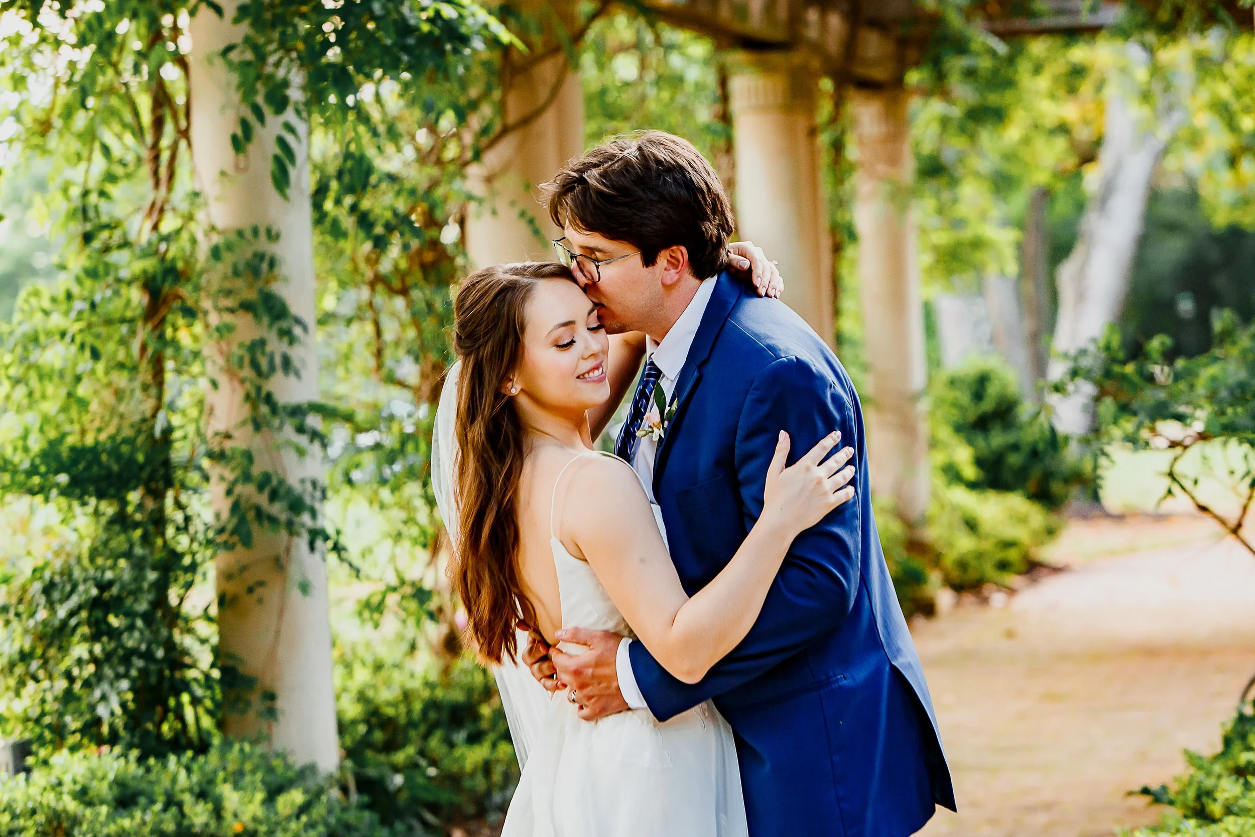groom kisses bride under vine arch