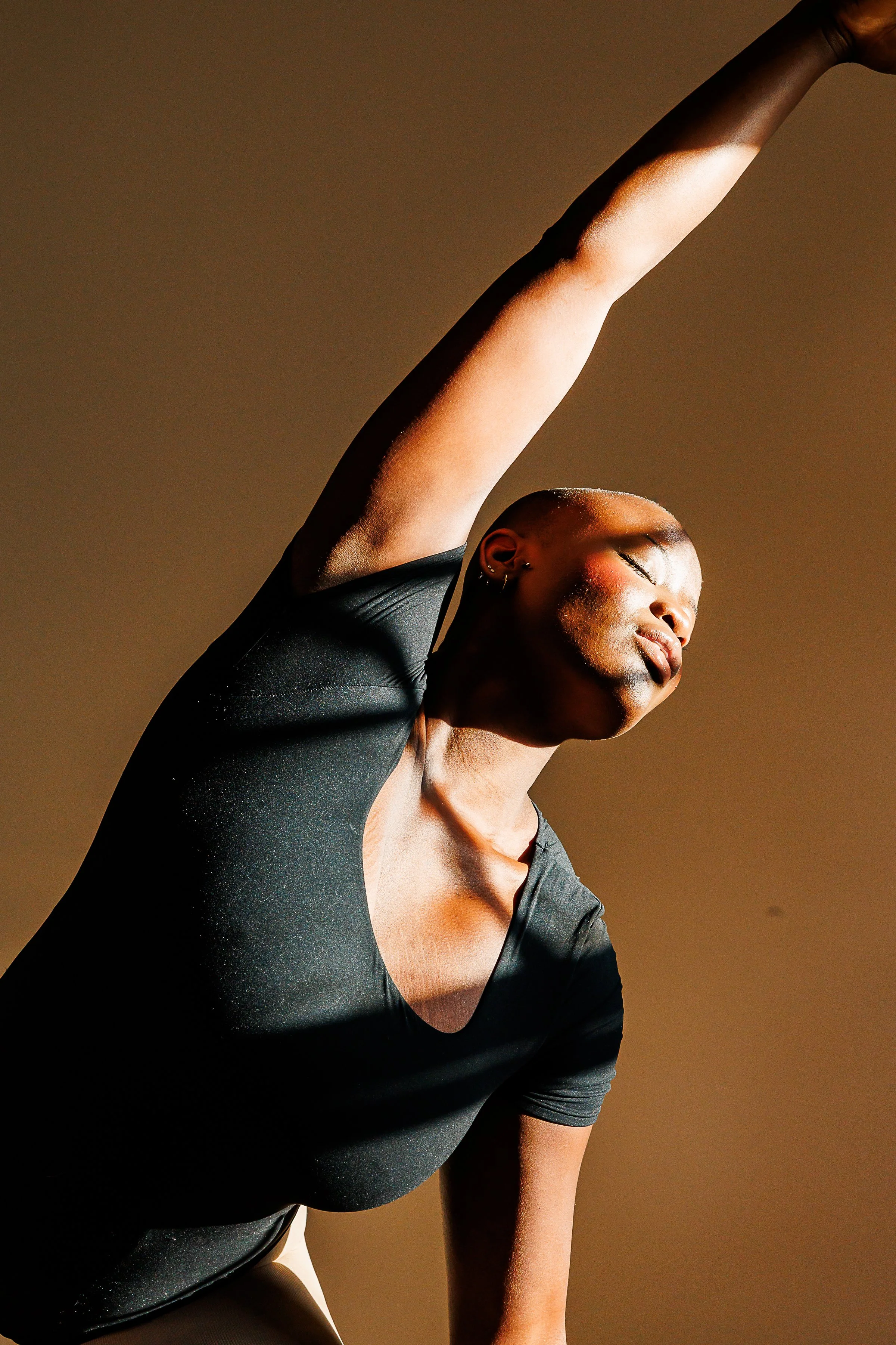 african woman in black t shirt stretching towards window light