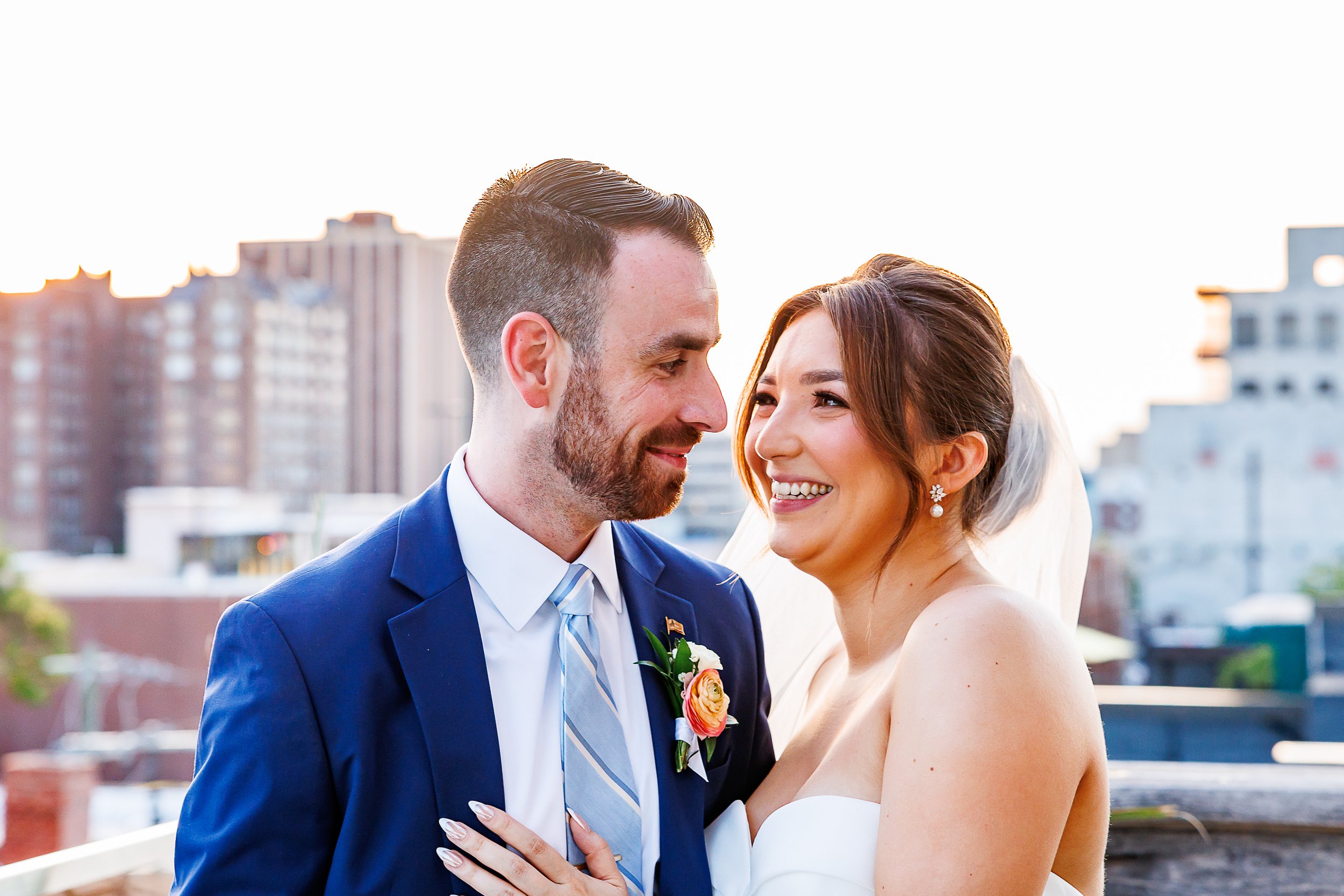 Bride and groom laughing together on the rooftop at Common House in Richmond, VA, with the city skyline glowing at sunset behind them.