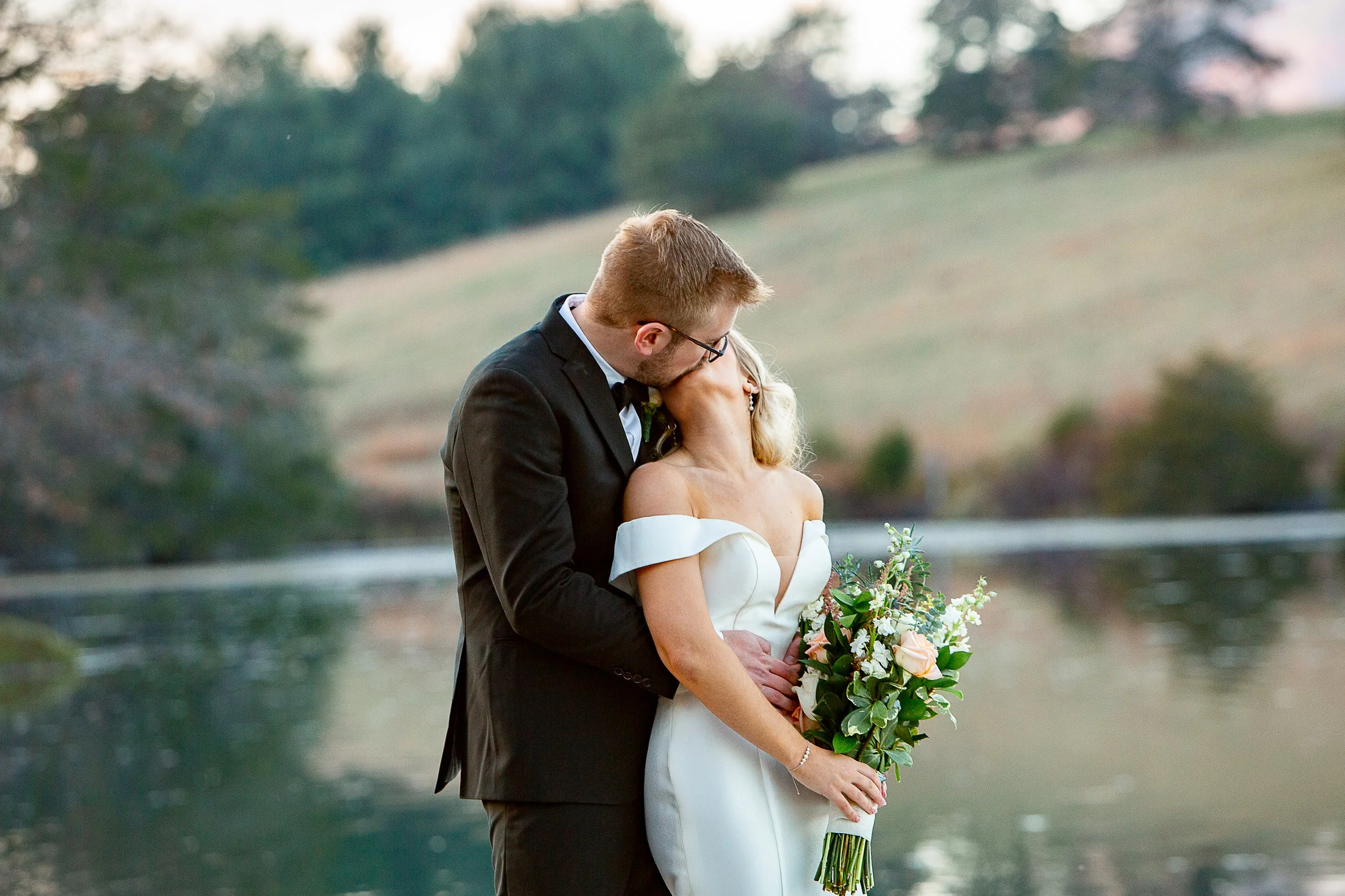 groom kissing bride from behind with lake in background