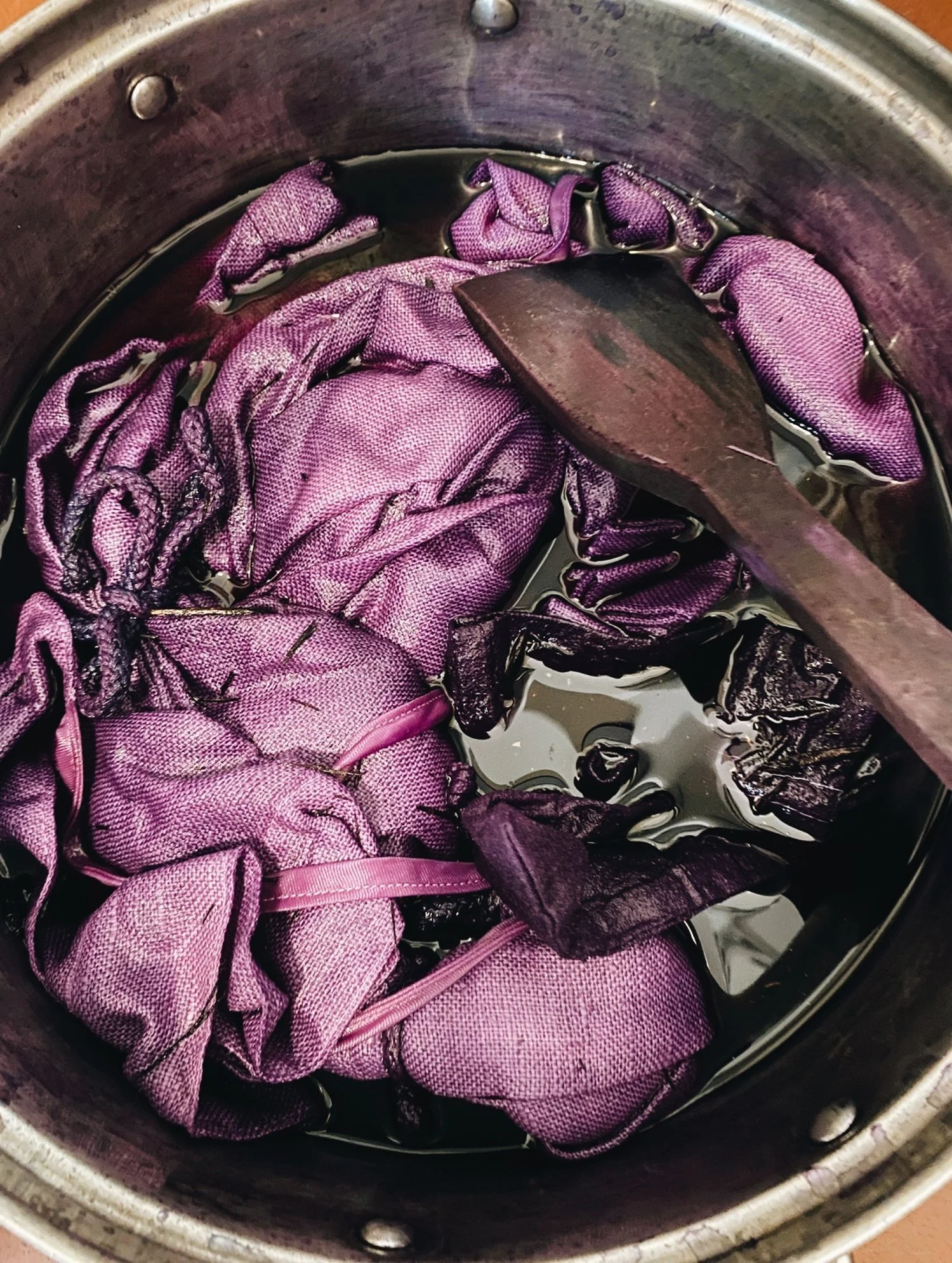 Purple fabric in boiling water in a pot, with a black cooking utensil. Natural dyeing with logwood to create a purple dye and to dye cotton fabric.