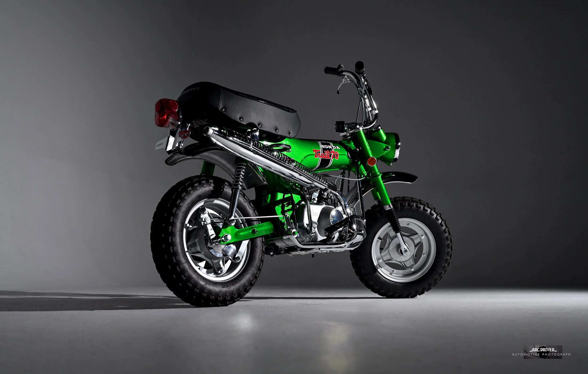 A vintage green Honda Trail 70 motorcycle with black seat and off-road tires, photographed against a dark gray background.