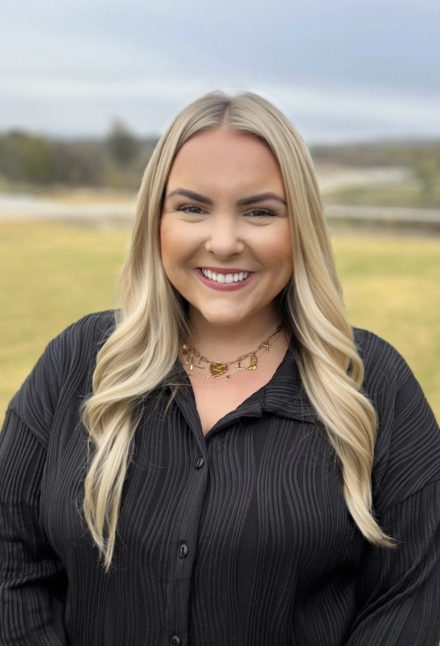 Person smiling in a casual setting with hoop earrings and a denim jacket.