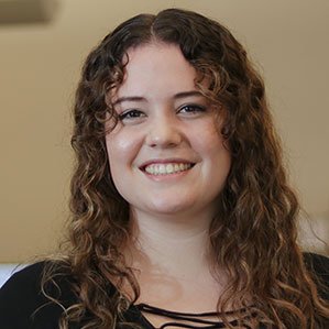 Person with curly brown hair smiling, wearing a black top, indoor background.