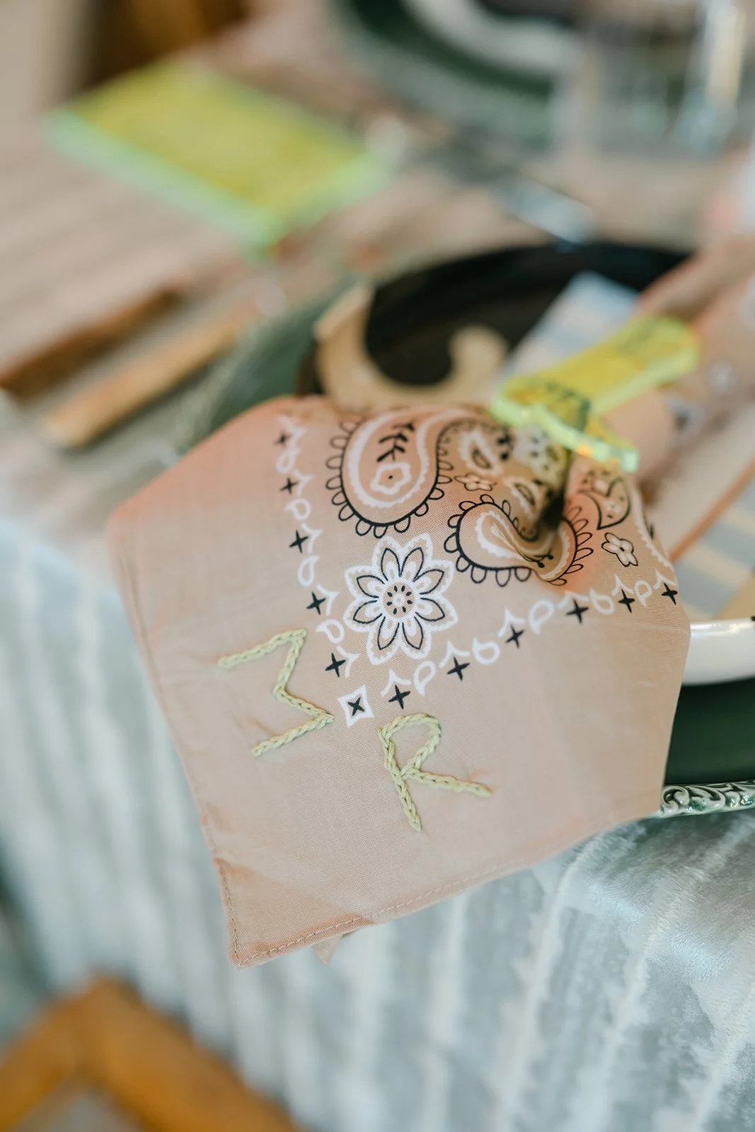 A pink bandana with white and black floral and paisley patterns, embroidered with the letters 'Z' and 'R', draped over a table.