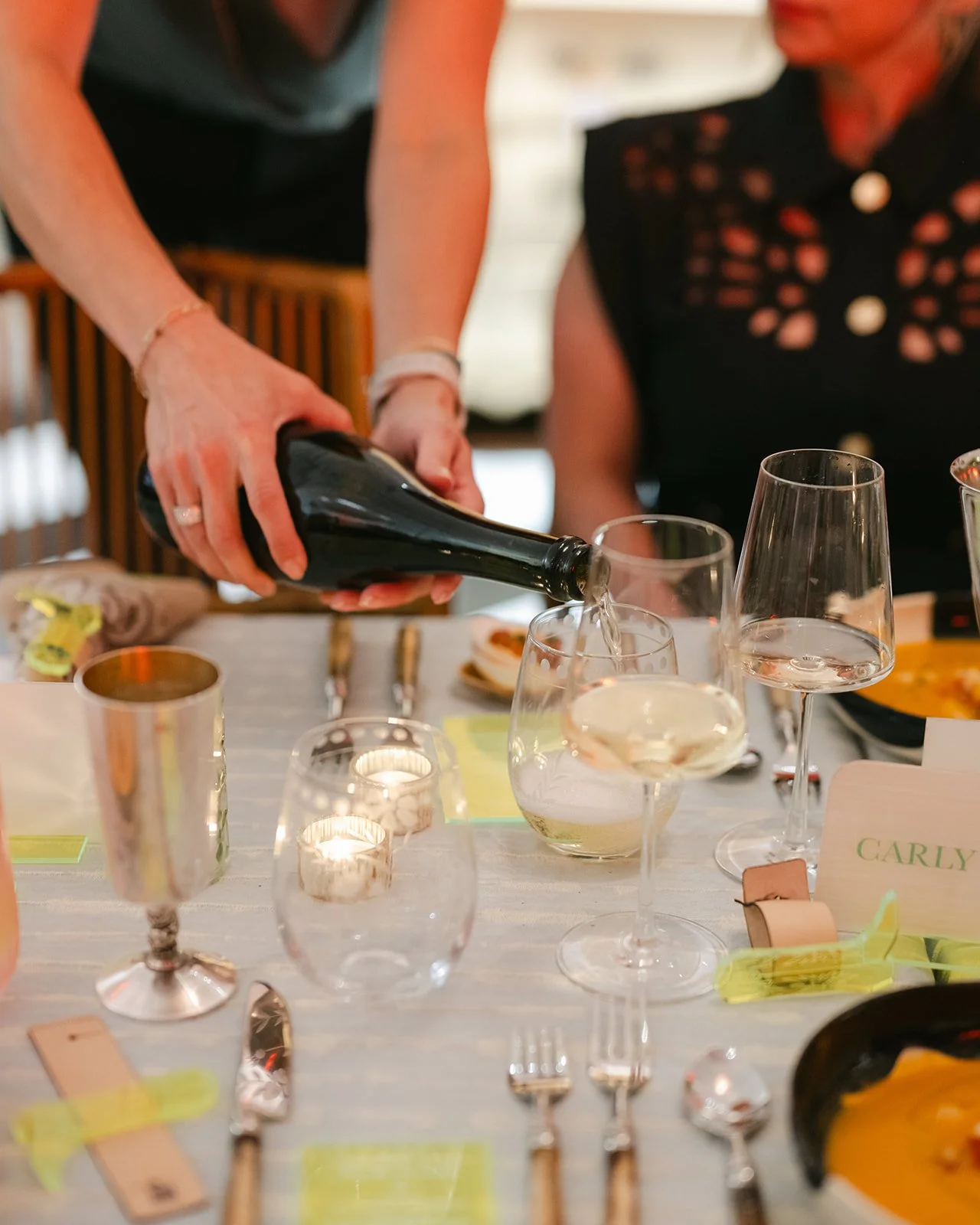 Person pouring sparkling wine into a flute glass on a table set for a meal