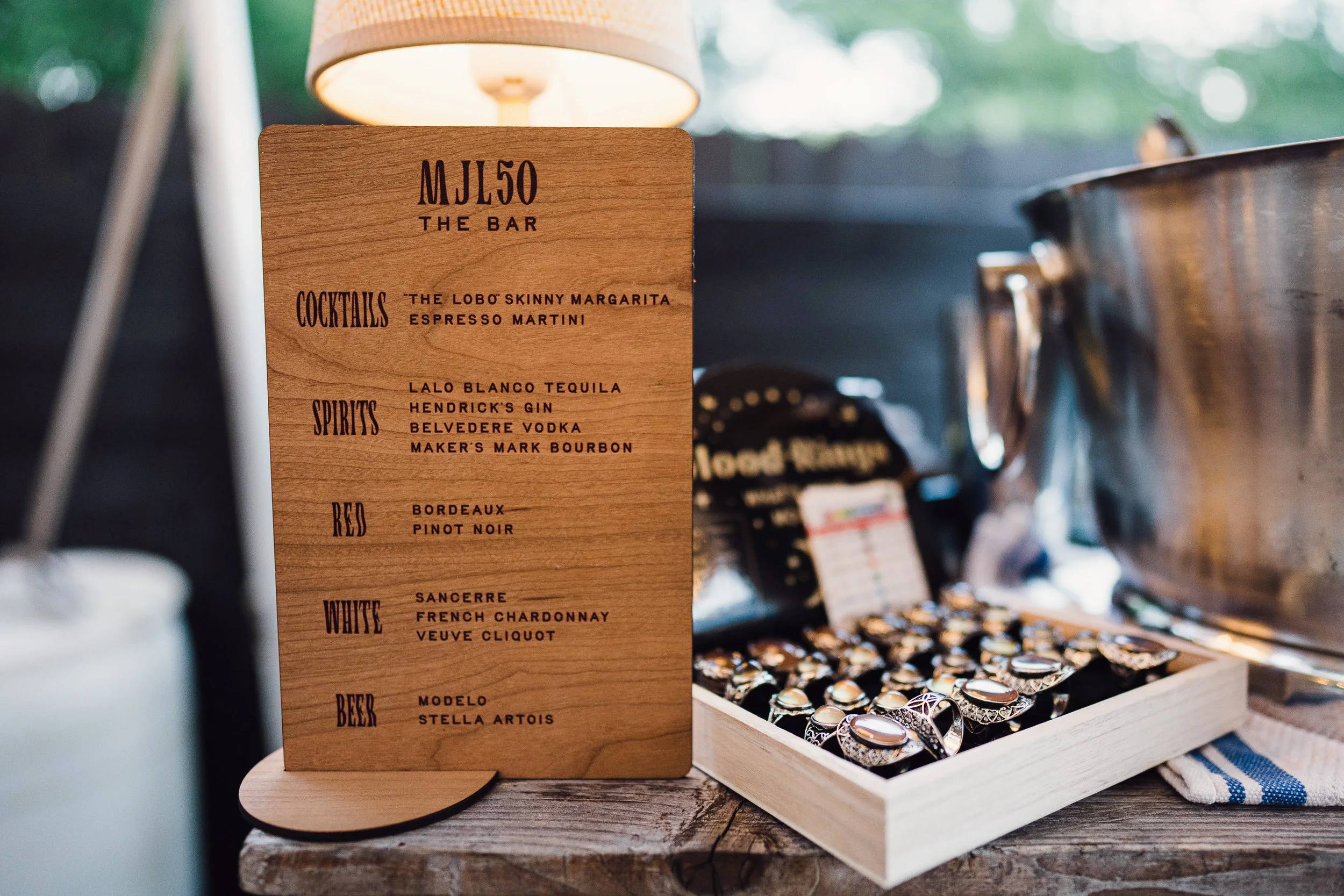 Indoor display of jewelry with a wooden menu stand listing various cocktails, spirits, wine, and beer options.