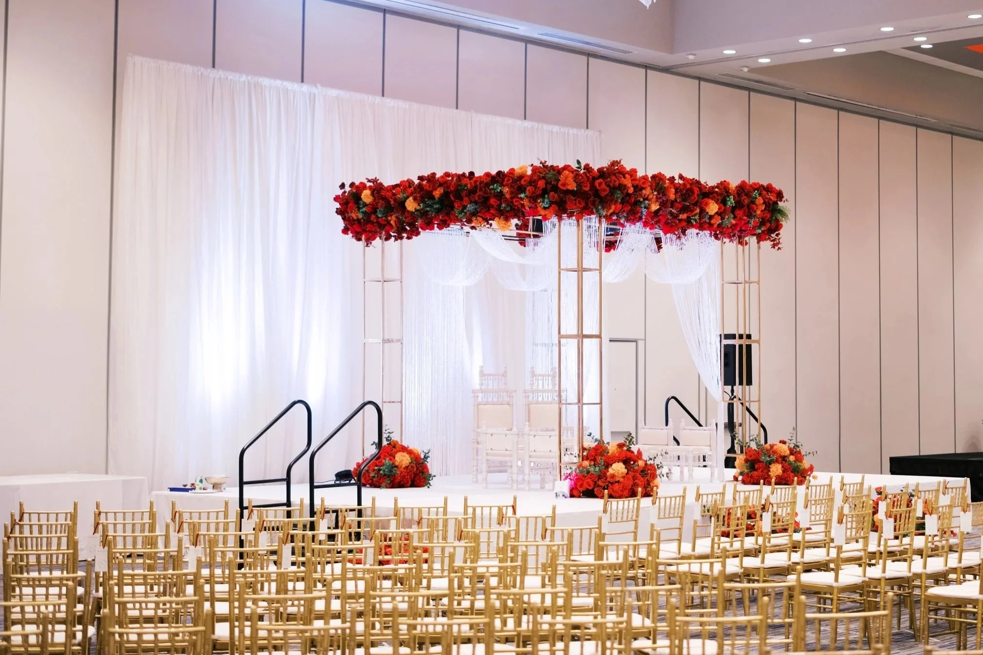 Luxurious wedding stage with ornate white and gold sofa, surrounded by decorative trees and draped curtains.