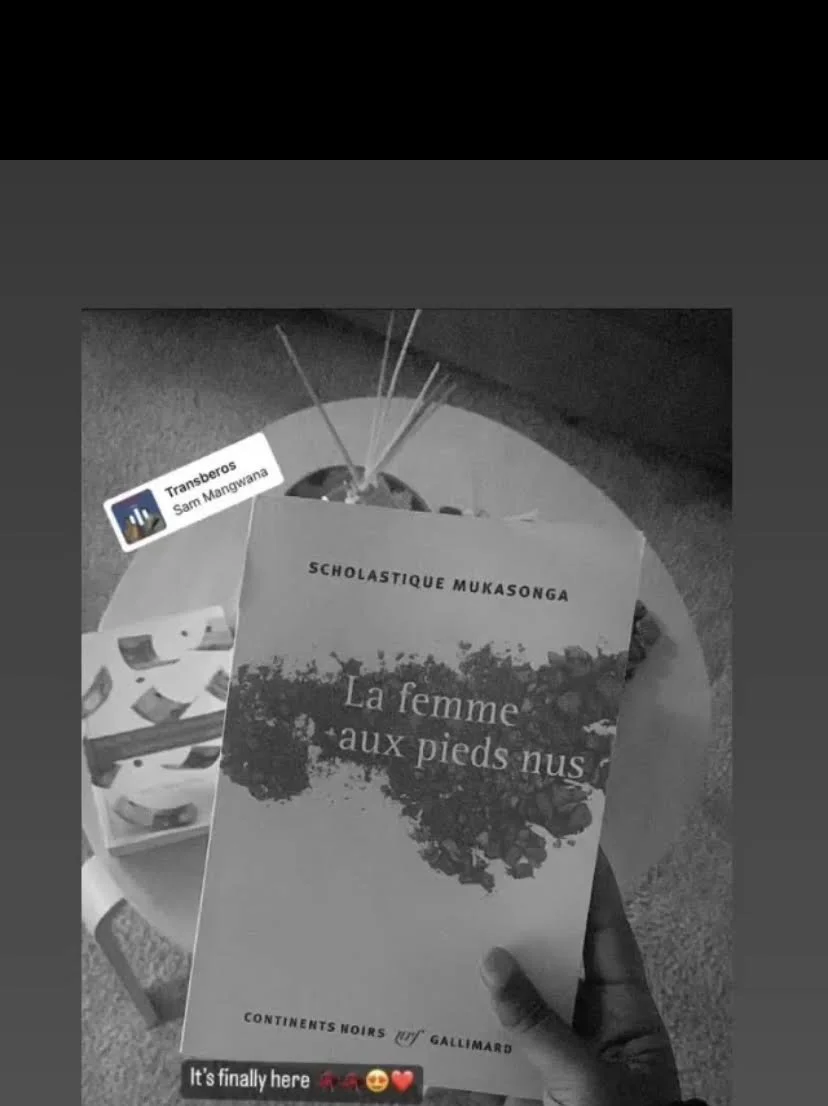 Hand holding a book titled 'La femme aux pieds nus' by Scholastique Mukasonga, with other books and pins in the background.