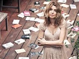 A woman sitting on the floor among scattered books and papers in a room.