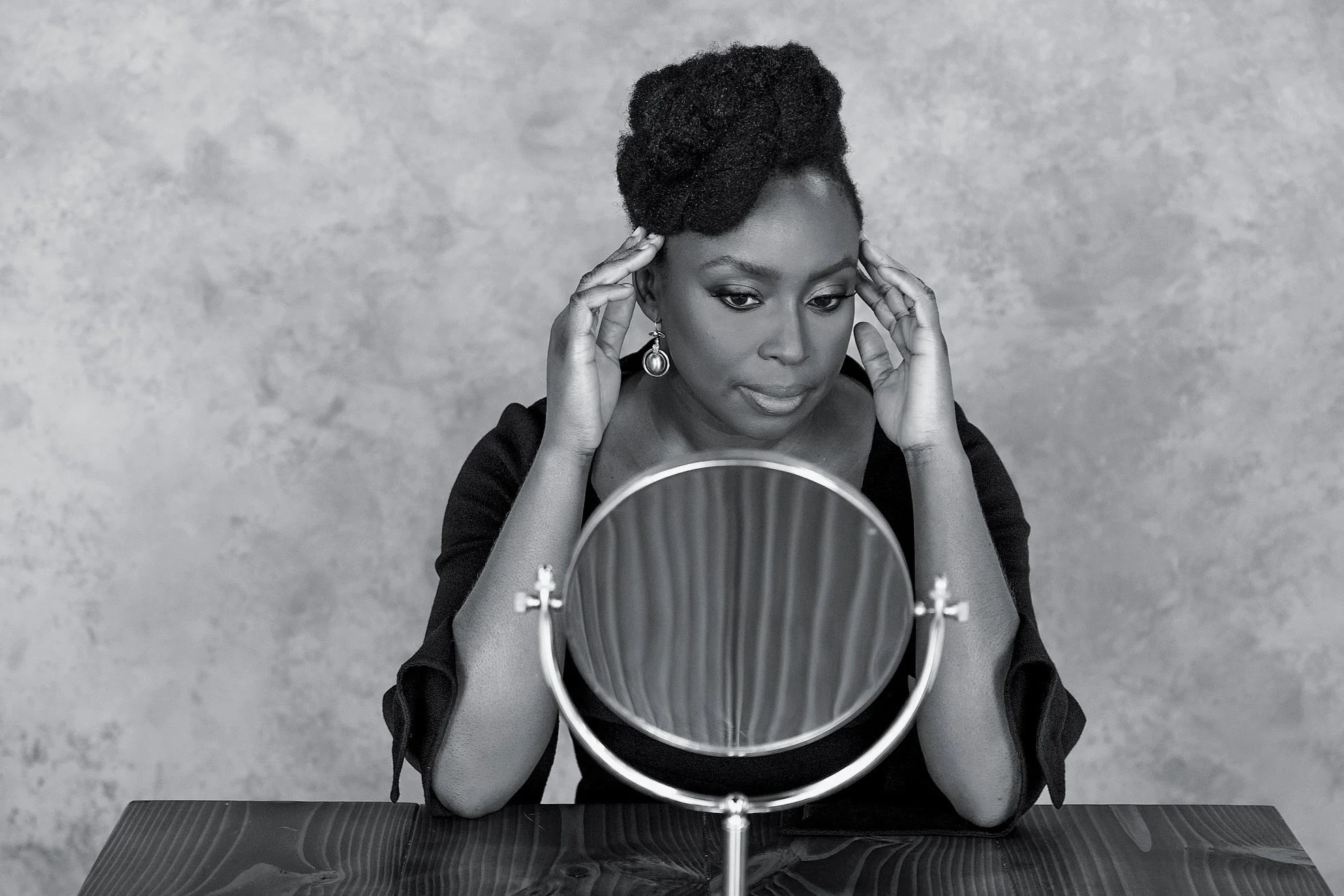 A woman with natural hair looking at her reflection in a tabletop mirror, with her hands on her temples.