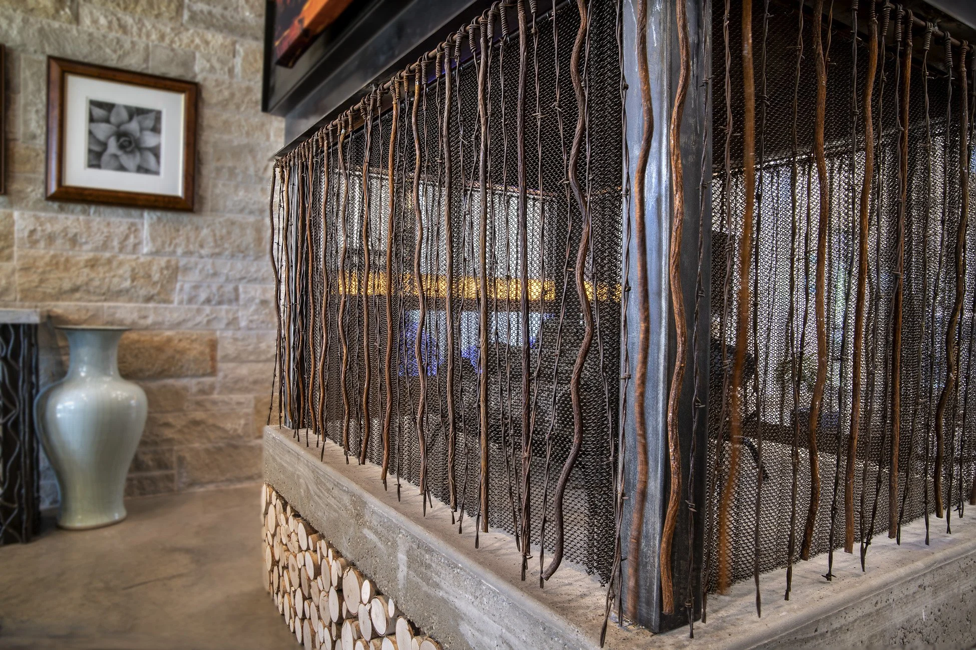 Close-up of a decorative fireplace with a metal grate and wood logs underneath, with a vase and framed flower photo on the wall in the background.