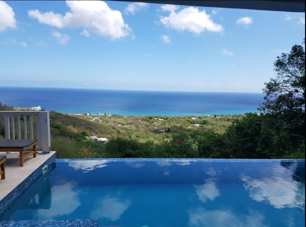 Infinity pool overlooking a lush green landscape and the ocean under a partly cloudy sky