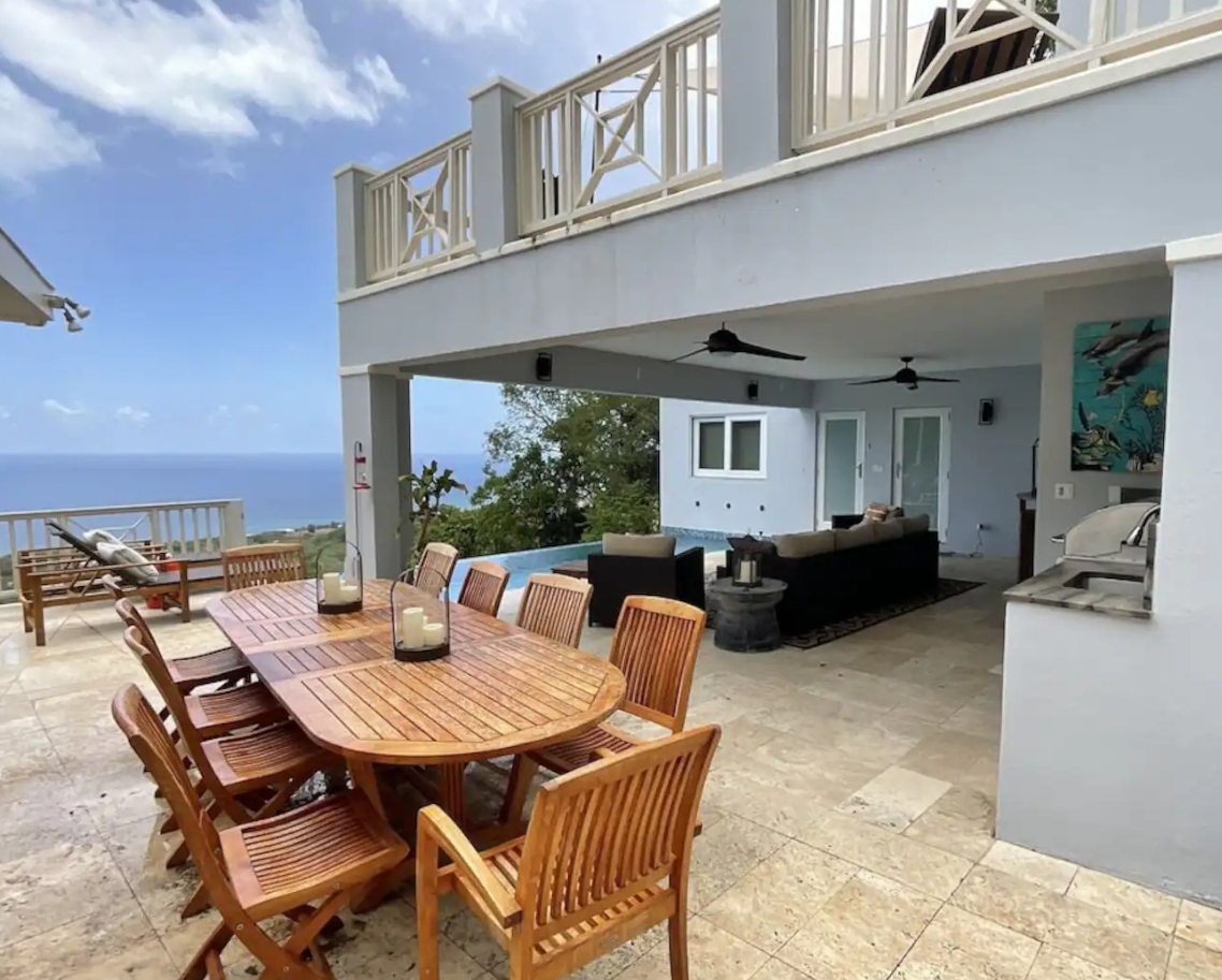Outdoor patio with dining table, chairs, and lounge seating with ocean view in the background.