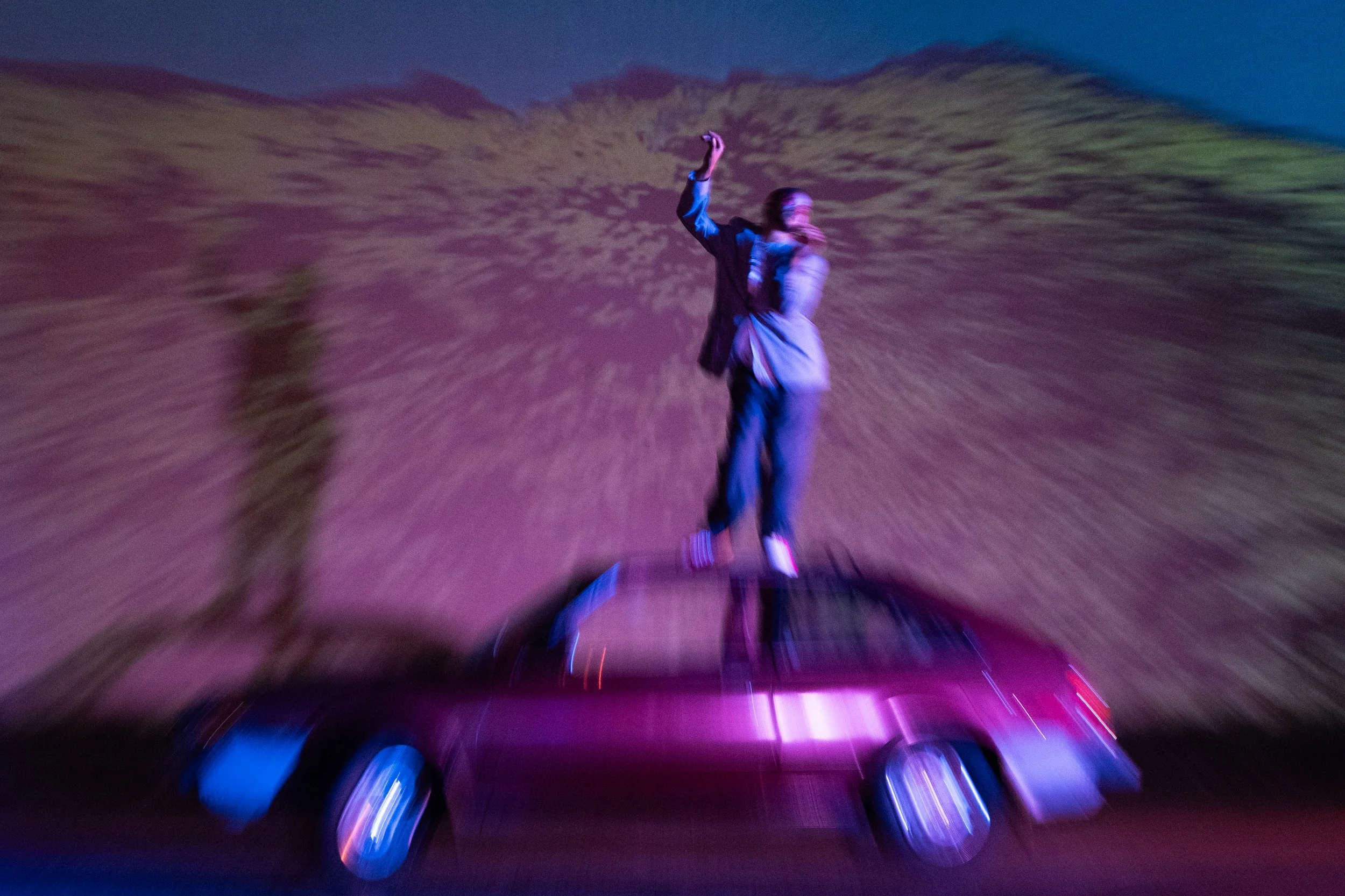 A person standing on a hoverboard with colorful LED lights, surrounded by moving lights and blurred surroundings, creating a dynamic, energetic scene at night.