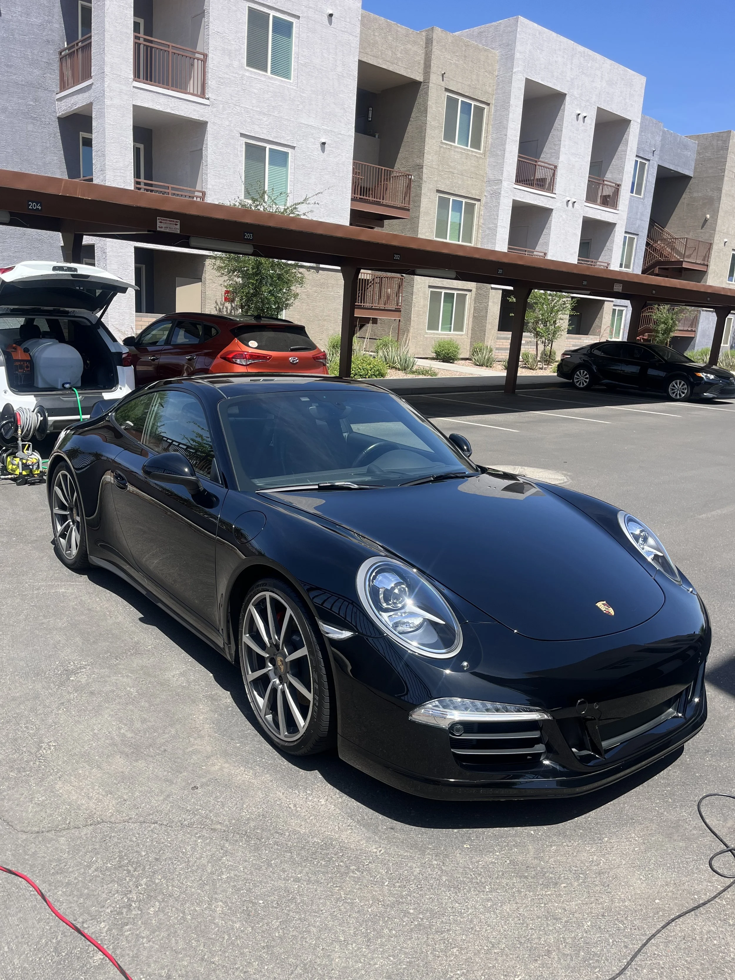 Black Porsche parked in a residential parking lot with an apartment building in the background after exterior detail in Mesa, AZ.