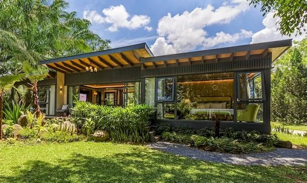 Modern house with large windows and a sloped roof, surrounded by greenery and a manicured lawn.
