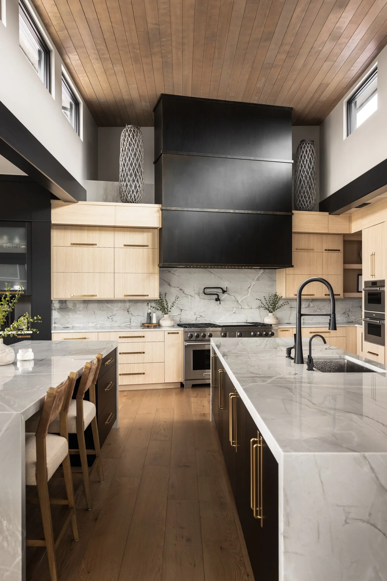 Modern kitchen with beige and black cabinetry, marble countertops, stainless steel appliances, and a wooden ceiling.
