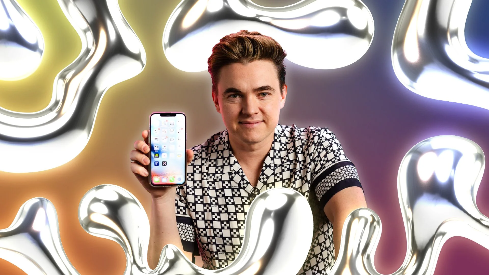 A man with styled hair holding a smartphone displaying a home screen, surrounded by shiny, abstract metallic shapes with colorful lighting in the background.