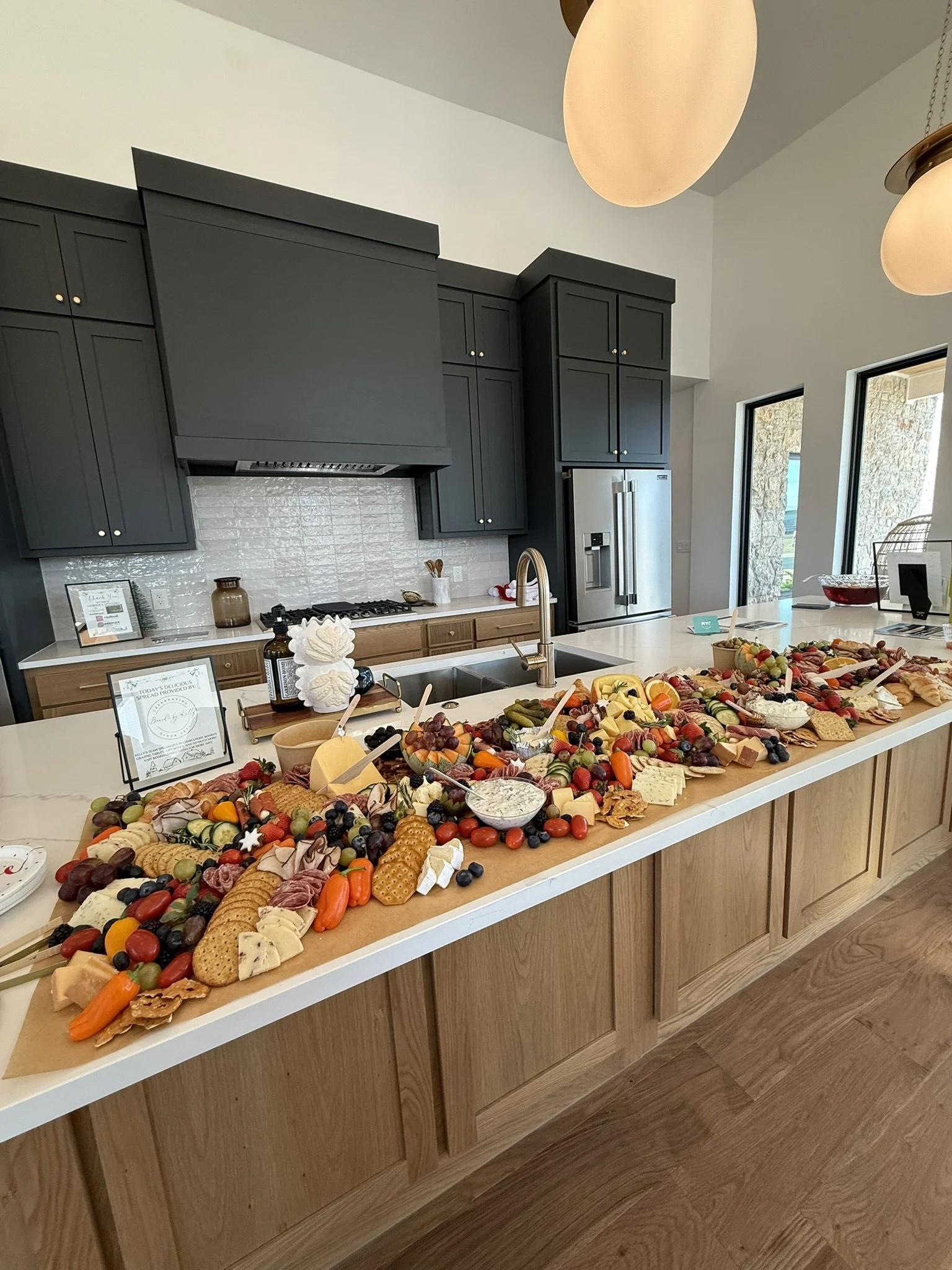 A kitchen island decorated with a large assortment of cheeses, fruits, crackers, and charcuterie for a gathering.