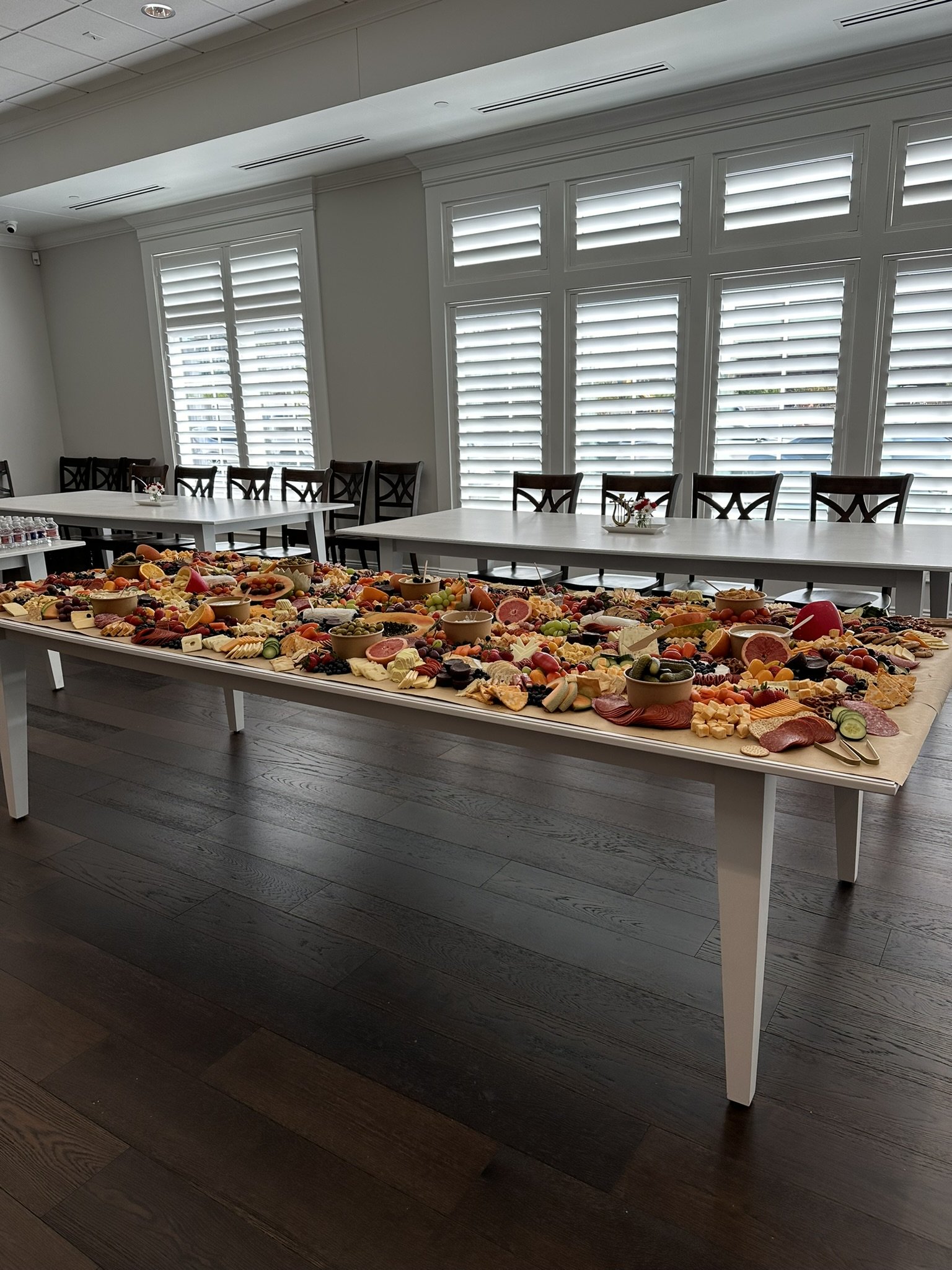 A charcuterie board arranged with an assortment of cheeses, cured meats, crackers, fresh fruits, and small bowls of dips and olives, displayed on table.