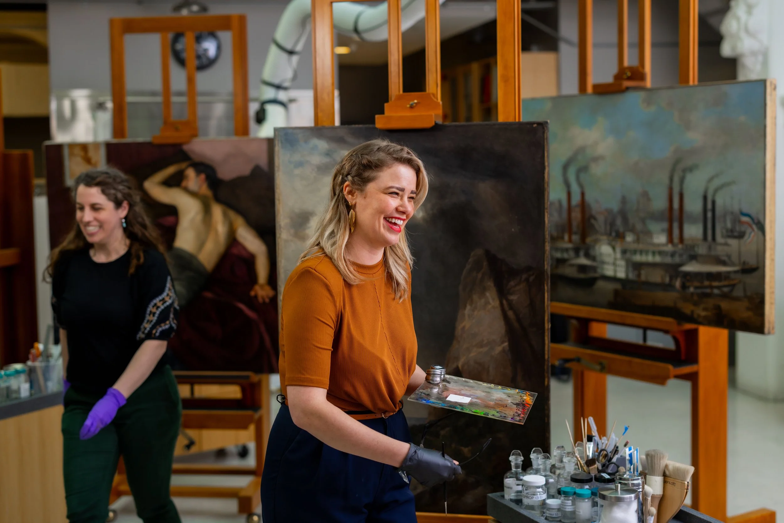 Women at an art studio working on paintings and mixing paint, smiling and laughing.