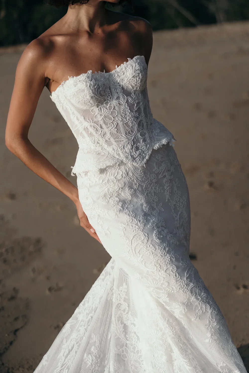 Begonia wedding gown featuring a sculpted corded Chantilly lace corset with curved hip detailing, paired with a fitted eco-silk or lace skirt with a dramatic train, and optional tulle layering or silk off-the-shoulder bows.
