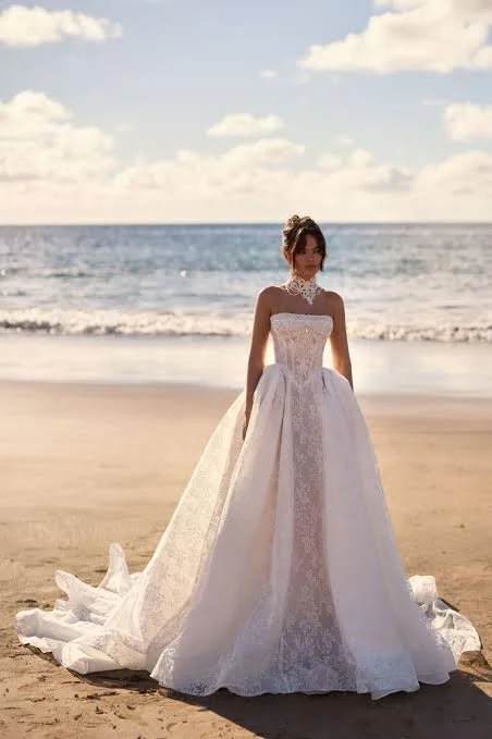 Vintage-inspired lace ballgown wedding dress featuring a structured boned corset with a straight neckline, shimmering Baroque-inspired lace, a full princess skirt with a sweeping train, detachable pearl embellishment, and optional matching lace choke