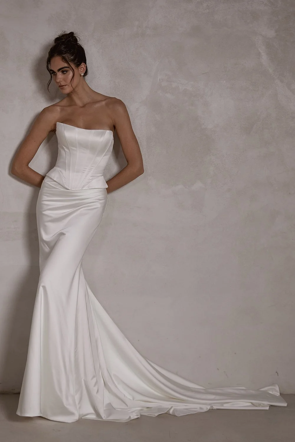 Cressida wedding gown featuring a structured boned corset with built-in cups, lace-up back, and a ruched silk satin mermaid skirt with a flowing train in off-white.