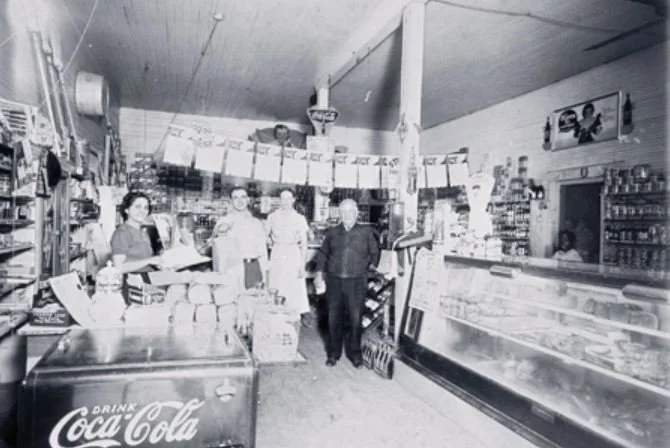 A historic photograph of an Italian family's shop in San Antonio, with shelves of goods and people behind the counter