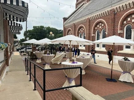 Cocktail tables with umbrellas and string lights on the brick patio