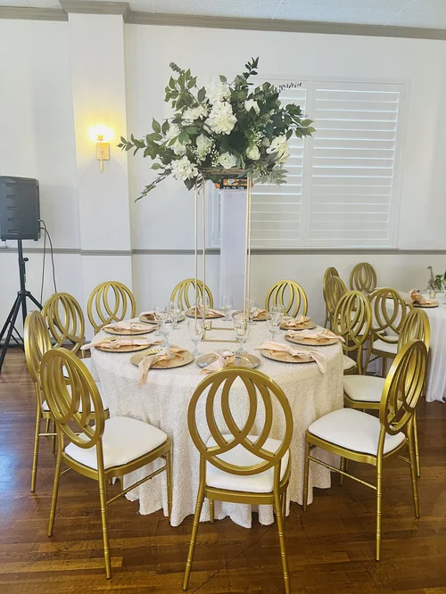 Round banquet table with gold chargers and a tall white floral centerpiece