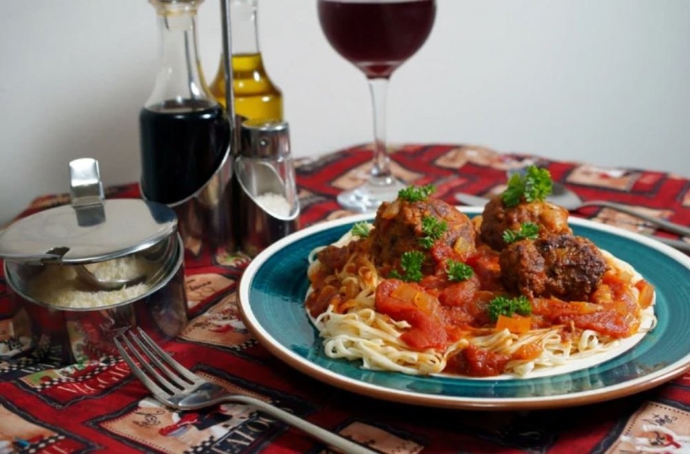 A plate of spaghetti and meatballs with a glass of red wine