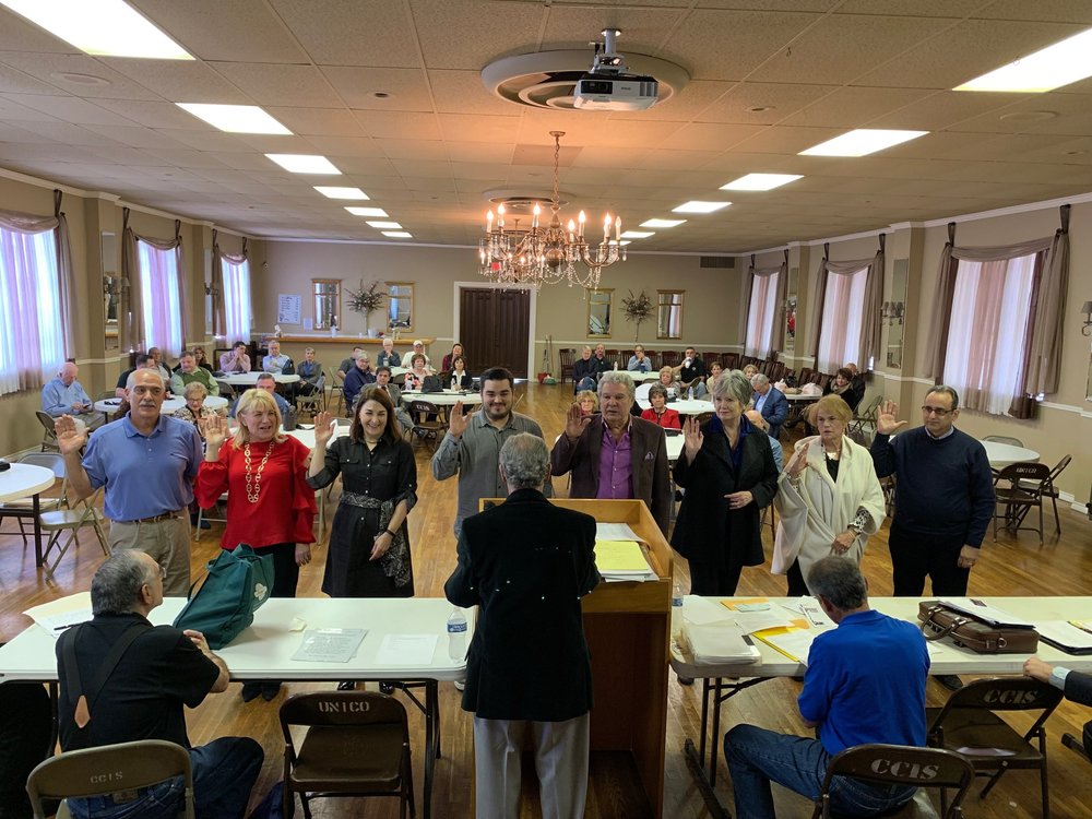 New members standing at the front of the hall during a meeting, with members seated at tables