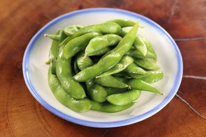 Plate of steamed edamame pods on a wooden board