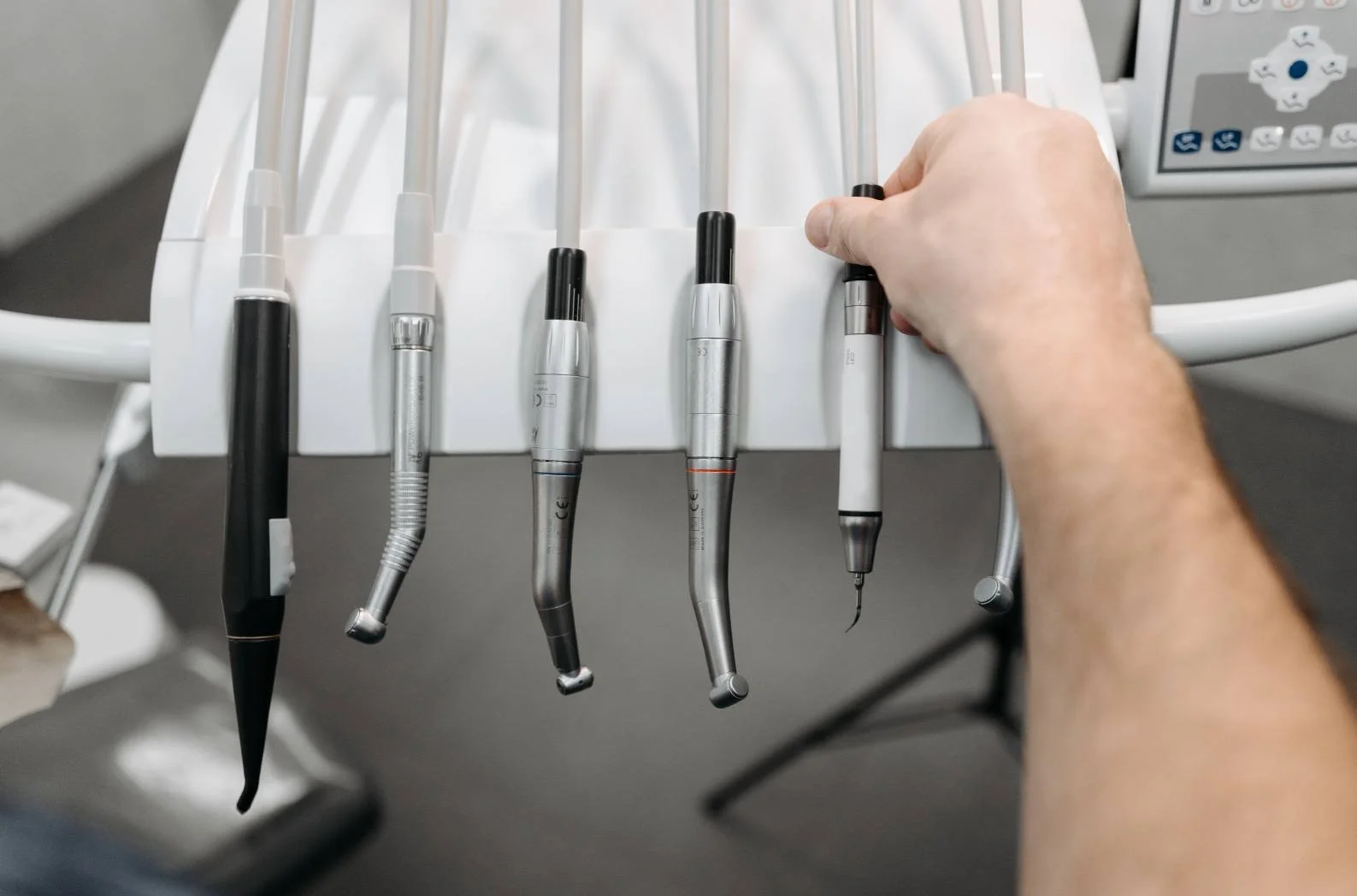 Hand reaching for dental handpieces lined up on a surgery delivery unit