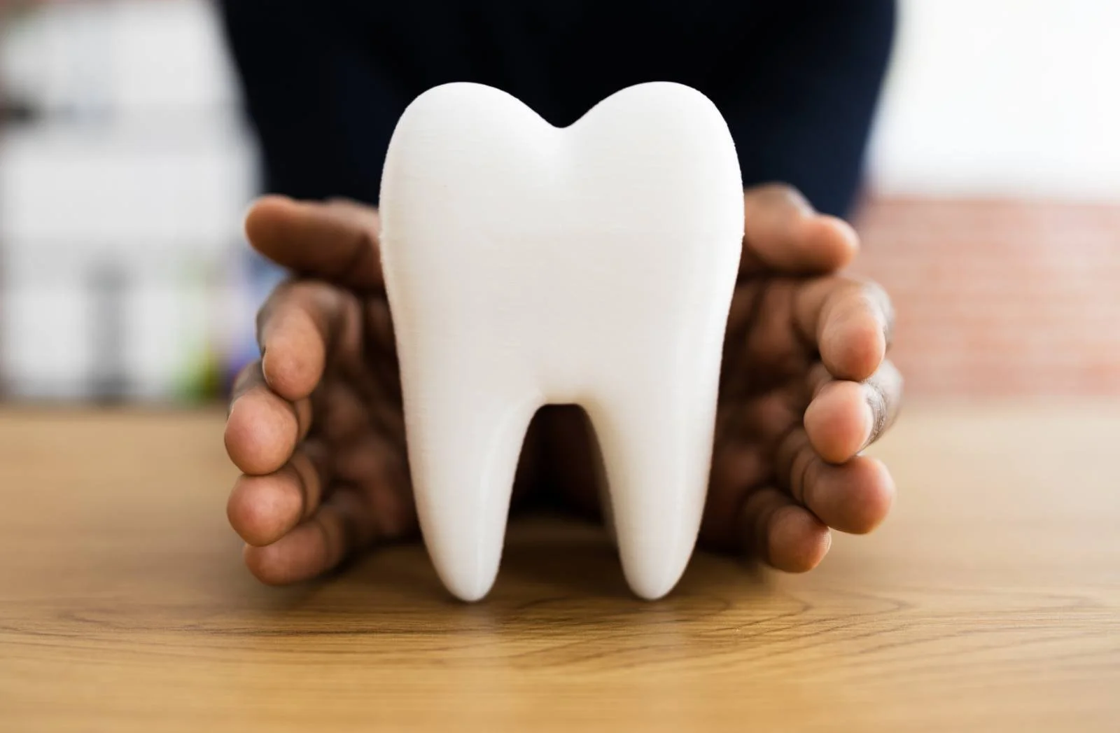 Hands cupped protectively around a large white model tooth on timber