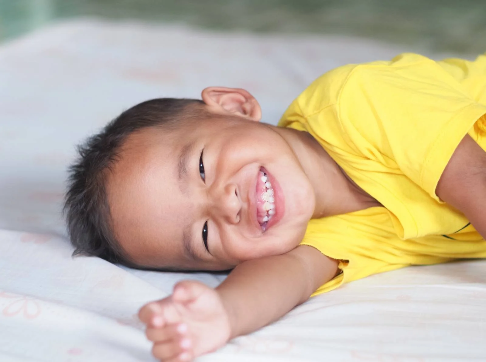 Baby in a yellow top lying on a bed and laughing