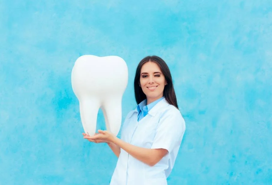 Dental assistant in uniform holding a large model tooth against a blue backdrop