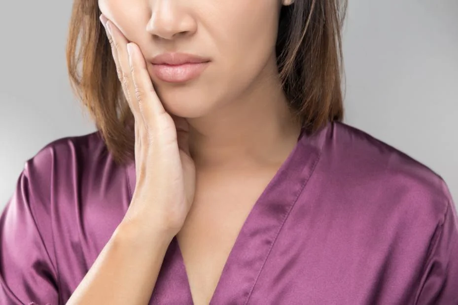 Woman in a purple robe holding her jaw with a pained expression