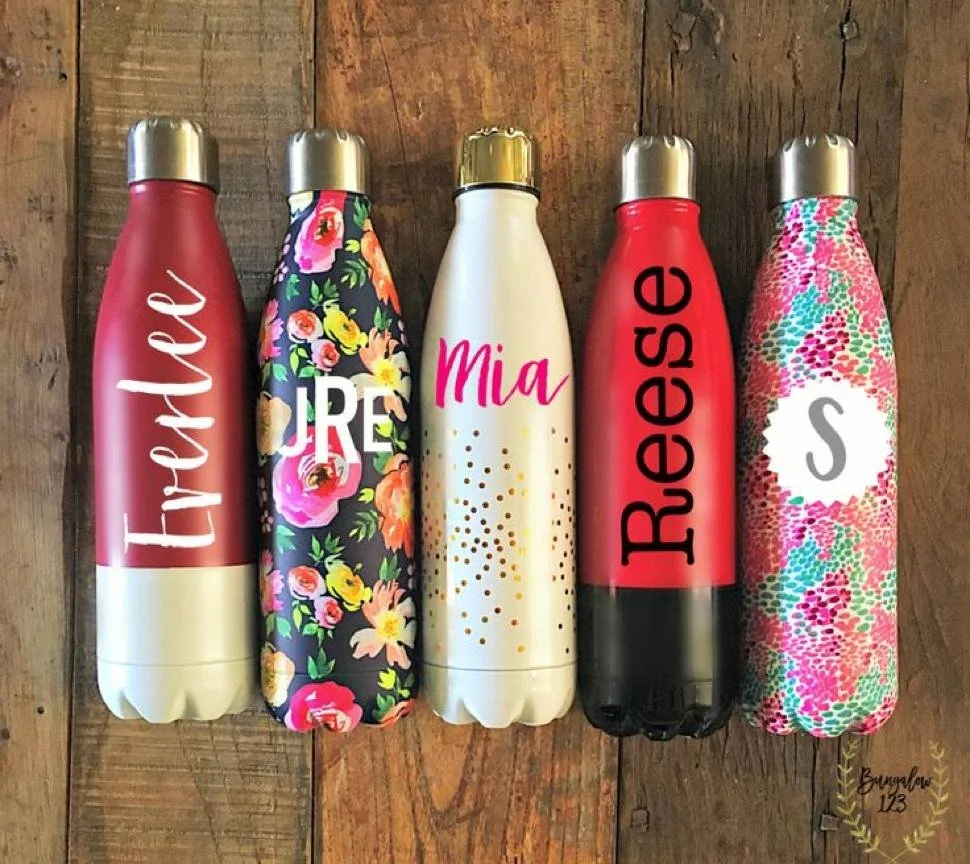 Five personalised stainless steel drink bottles standing on a timber bench