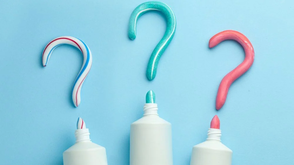 Three toothpaste tubes squeezed into question mark shapes on a blue background