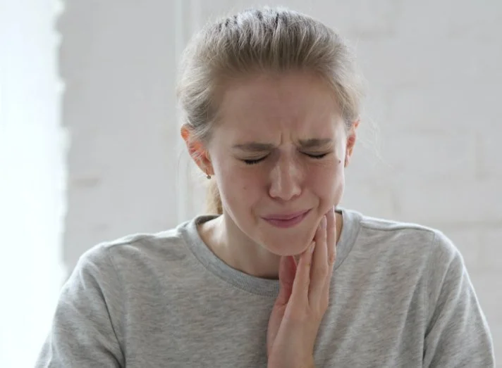 Woman screwing up her face and clutching her jaw in pain