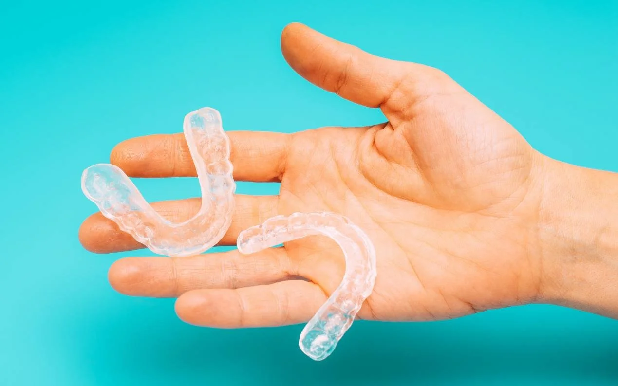 Two clear plastic splints resting on an open palm against turquoise