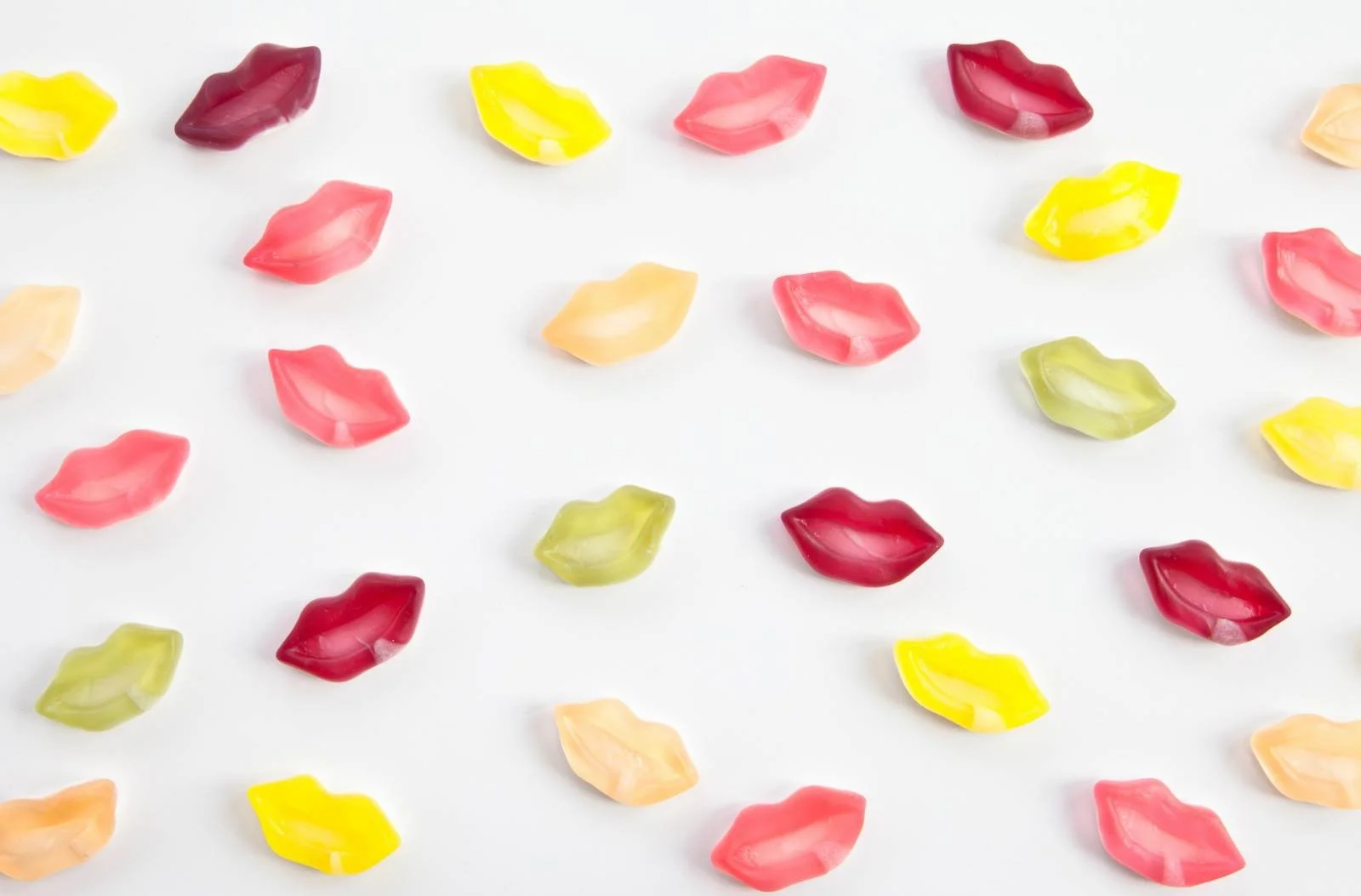 Rows of brightly coloured lolly lips scattered on a white surface