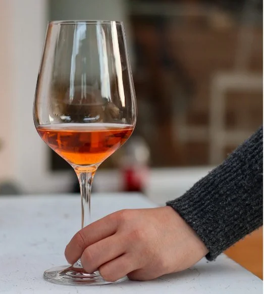 Glass of amber wine on a bench with a hand resting alongside
